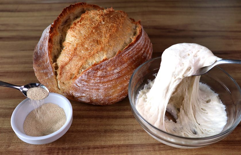 Um pão caseiro atrás de um pote com fermento biológico e outro com fermento natural